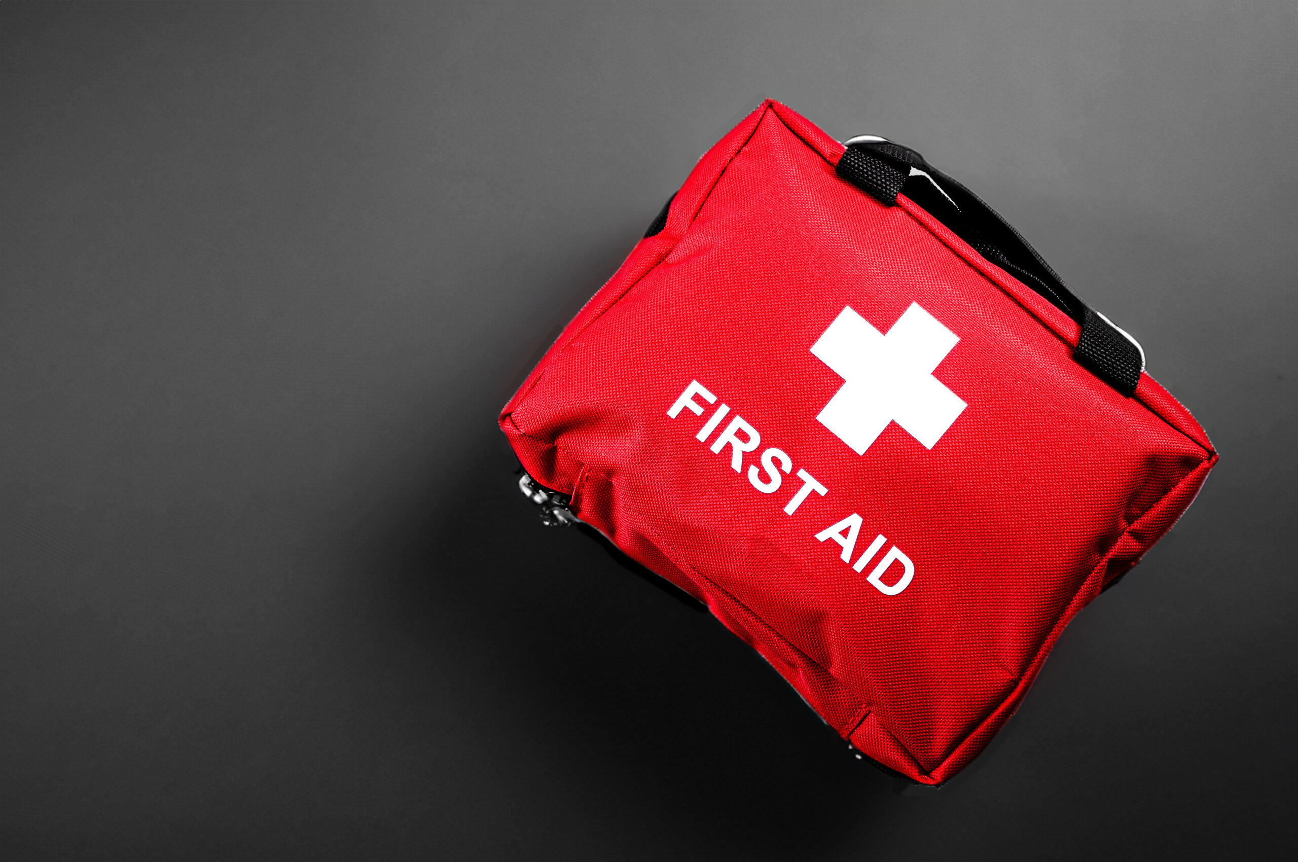 First aid treatment and medical emergency response concept with flat lay view of a red with a white cross first aid kit isolated on black background